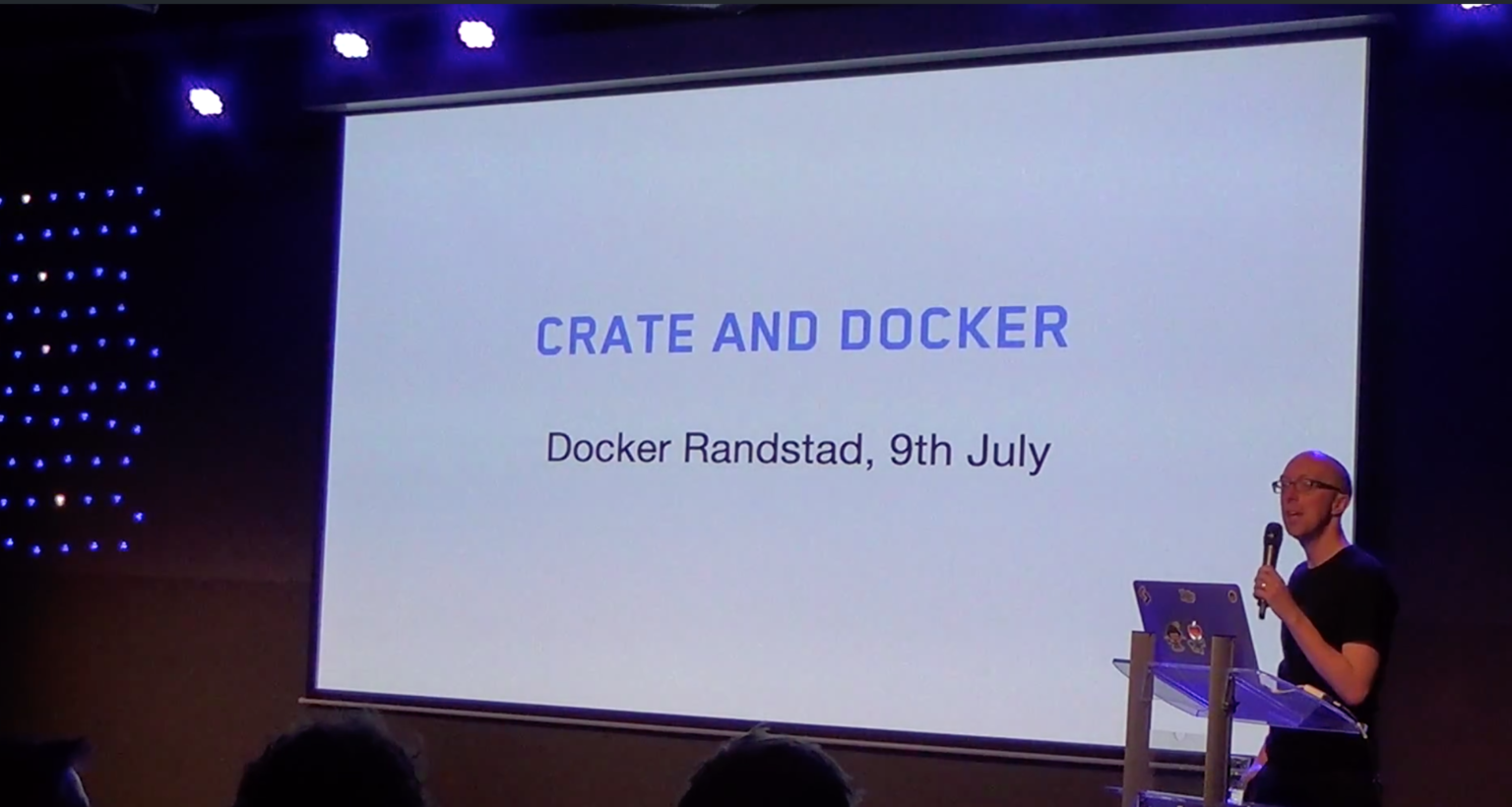 A presenter standing in front of a projection where it says CrateDB and Docker